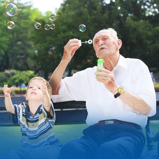 Older man and young boy, sitting on a park bench and blowing bubbles.